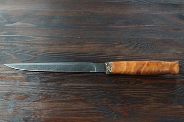 hunting knife from Damascus steel on wooden background