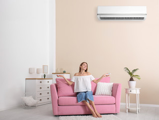 Happy young woman sitting under air conditioner at home