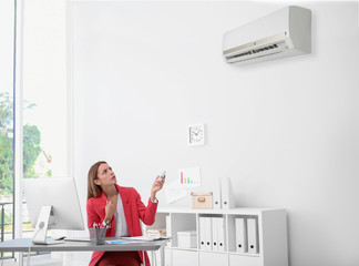 Young woman suffering from heat under broken air conditioner in office