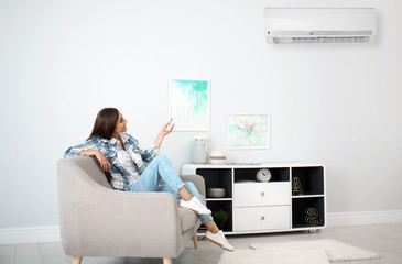 Young woman with air conditioner remote at home