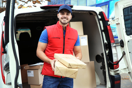 Young courier with parcels near delivery van outdoors