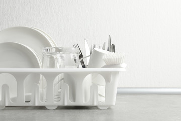Drying rack with clean dishes and cutlery on table near white wall. Space for text