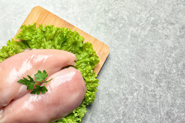 Wooden board with raw chicken breasts and lettuce on grey background, top view. Space for text