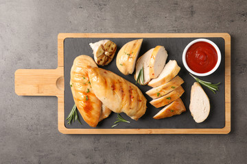 Board with fried chicken breasts and sauce on grey background, top view