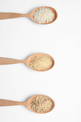 Spoons with different types of uncooked rice on white background, top view