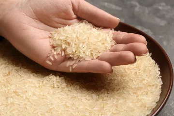 Foto auf Acrylglas Woman holding grains near plate with parboiled rice on table, closeup © New Africa