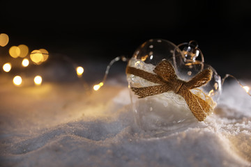 Glass heart and fairy lights on white snow outdoors. Space for text