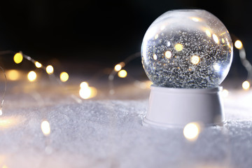 Crystal globe and Christmas lights on white snow outdoors. Space for text