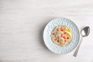Plate of quinoa porridge with orange, banana and pomegranate seeds near spoon on white wooden background, top view. Space for text