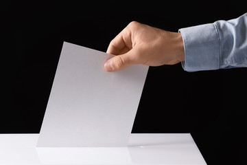 Man putting his vote into ballot box on black background, closeup