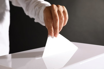 Woman putting her vote into ballot box on black background, closeup
