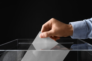 Man putting his vote into ballot box on black background, closeup