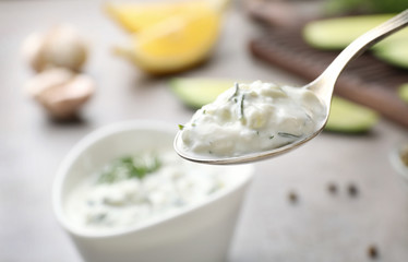 Spoon of cucumber sauce against blurred background, space for text. Traditional Tzatziki
