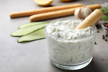 Bread stick in bowl of cucumber sauce with ingredients on grey background, space for text. Traditional Tzatziki