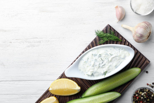 Tzatziki sauce with lemon, cucumber, dill and pepper on white wooden background, top view. Space for text