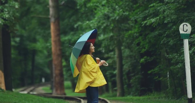 Young Caucasian girl having a walk in the nice park with an umbrella under the rain and spinning around.