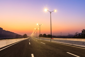 City road and bright street lights landscape at sunset