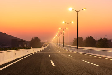 City road and bright street lights landscape at sunset
