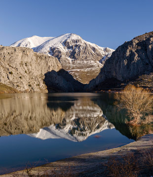 An calm lake reflecting snowy mountains of Leon, Spain on its shores as well as a blue sky above
