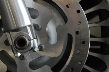 Close-up of motorcycle wheel, shows partial view of wheel, tire, rotor, and forks.