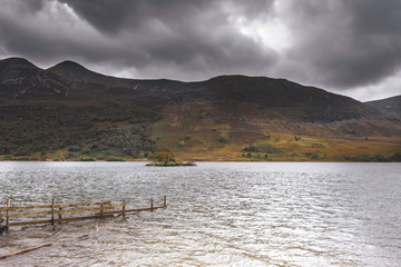 Scenic landscape of Cumbria,Uk.Lake with isle, mountain, moody sky, flooded fence.No people and copy space. 