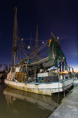 Back of a fishing boat tied to dock with calm water as sun sets leaving a purple sky