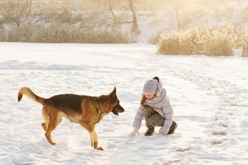 Cute girl and German shepherd for a walk. Sunny winter day. Girl playing with pet