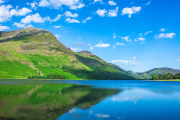 Fototapeta na wymiar Beauty of british countryside in spring.Green mountain reflecting in crystal clean lake surface and blue sky with few clouds above horizon.