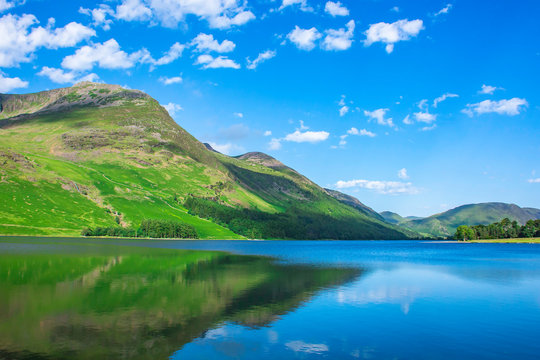 Beauty of british countryside in spring.Green mountain reflecting in crystal clean lake surface and blue sky with few clouds above horizon. © Jazzlove