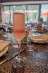 Glass of Champagne (wine sparkling) cocktail next to Glass with water and cutlery and  dinnerware on wodden table in restaurant. Vertical photo.
