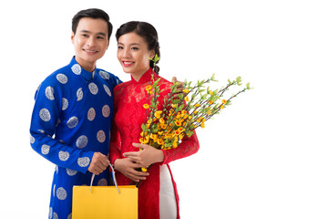 Portrait of positive Vietnamese couple with branches of blooming apricot and paper-bag