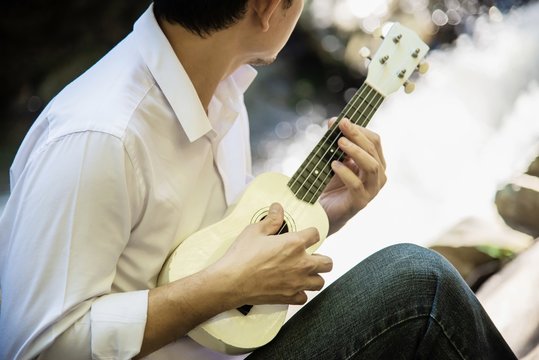 Man play ukulele new to the waterfall - people and music instrument life style in nature concept