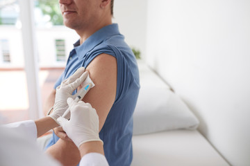 Doctor injecting vaccine in arm of male patient in hospital