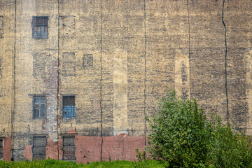 A large mesh covers the old brick wall. The facade of an abandoned building with windows. Weathered dirty dark yellow brickwork with cracks. Grungy surface. Perfect for urban background and design.