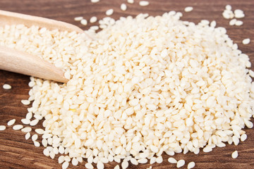 Heap of sesame seeds with wooden scoop on board