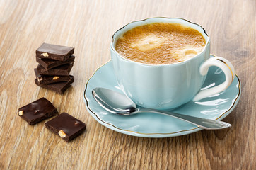 Coffee espresso in cup, spoon on saucer, pieces of chocolate on table