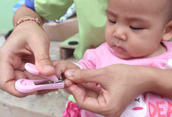 The Asian mother is cutting the nails for the daughter.