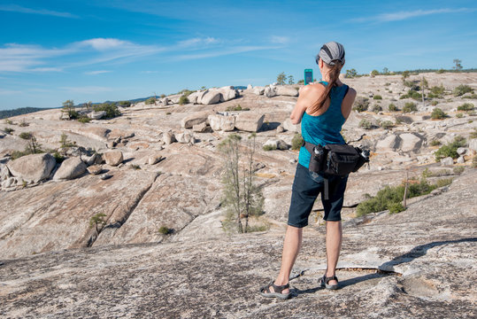 Older, woman hiker in rocky landscape taking picture on cell phone