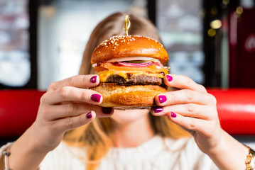 Young girl holding in hands fast food burger with cutlet, cheese and red onion.