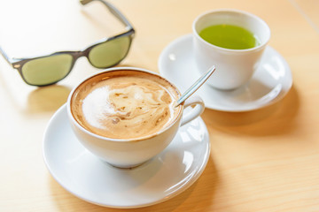 hot cappuccino coffee with green tea and sunglasses on table