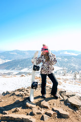 young woman is holding snowboard, standing on rock. Ski resort.