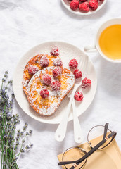 Afternoon tea break rest table - french toast with fresh raspberry, green tea and book on light background, top view. Flat lay
