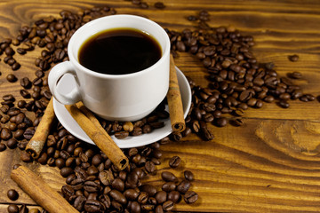 Cup of coffee, roasted coffee beans and cinnamon sticks on wooden table