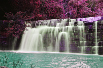 The beautiful waterfall in purple forrest down to emerald green lake. Striking nature.