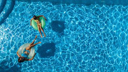 Active children in swimming pool aerial top view from above, happy kids swim on inflatable ring donuts and have fun in water on family holiday vacation on resort

