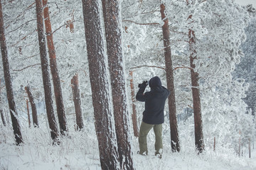 man in the hood photographs snow-covered pines in the winter forest