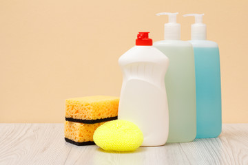 Bottles of dishwashing liquid and sponges on beige background.