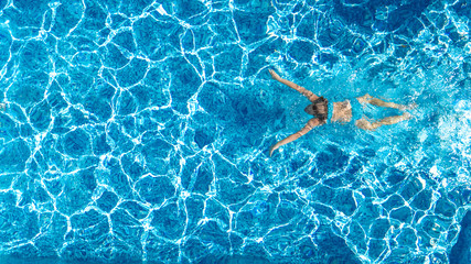 Active girl in swimming pool aerial drone view from above, young woman swims in blue water,...