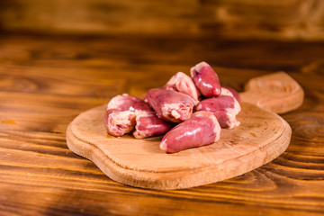 Cutting board with raw chicken hearts on wooden table