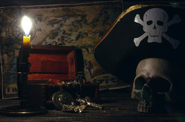 Pirate map and treasure chest with a gold and human skull in captain hat on a pirate captain table...
